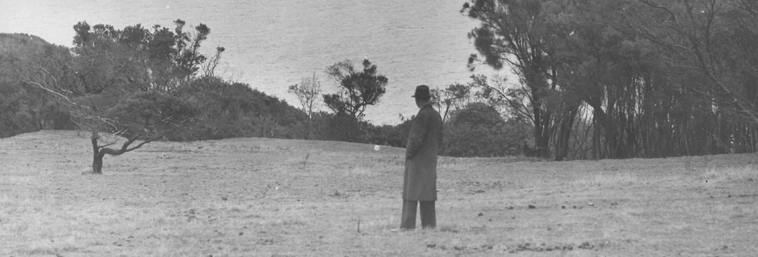 black and white photo of a man looking out over a field of trees and grass