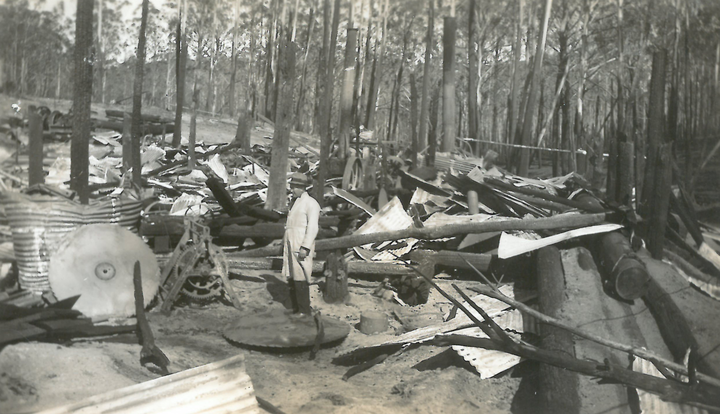 black and white photo of burned hut with man looking on
