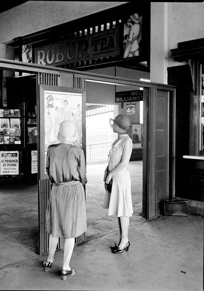 Women in 1920s/30s clothes looking at a sign 