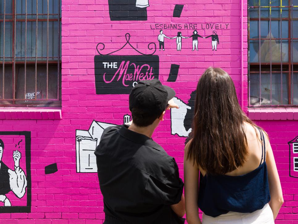 Two people looking at a mural painting on the wall of a building