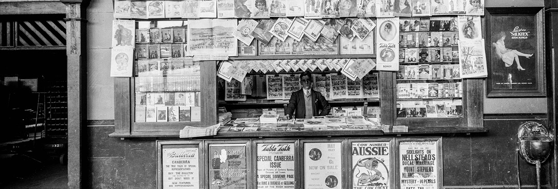 Black and white image of man working at newspaper stand, Spencer St train station