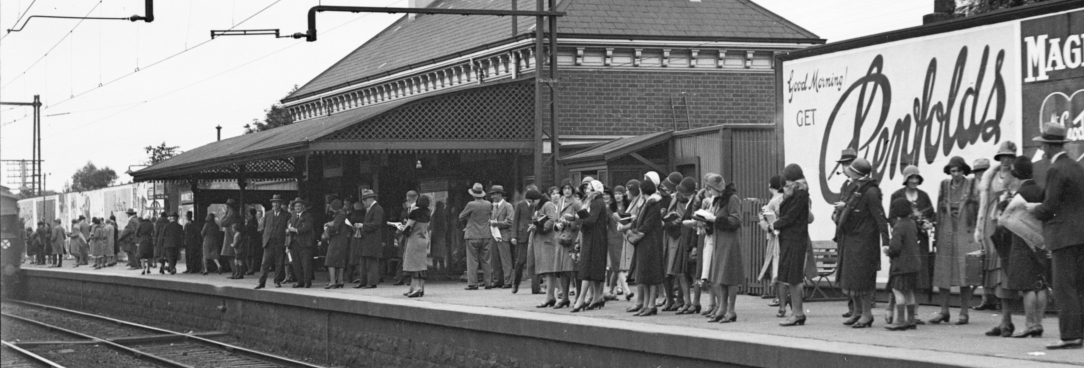 Black and white photo of people waiting on a railway station platform