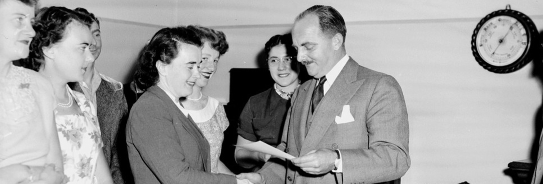 black and white photo of a man handing our certificates to a group of women