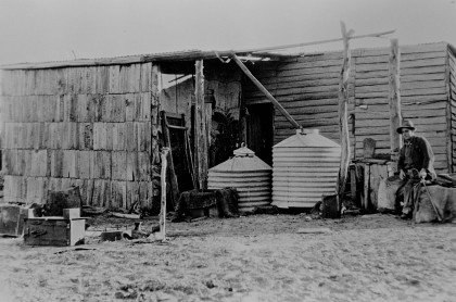 Man in hat sitting outside a farm shed