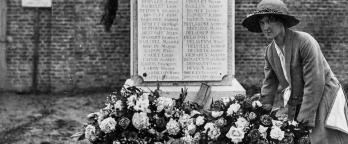 Black and white photo, woman lays flowers at a memorial
