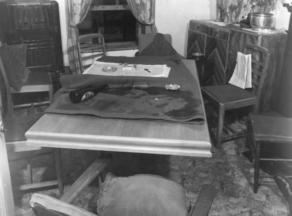 black and white photo of a messy room with dining table and chairs, spilled beer and blood spatter