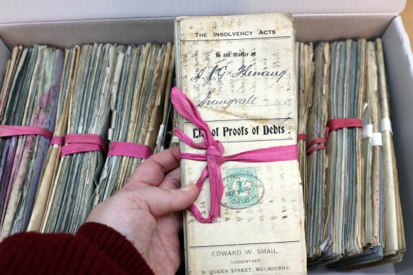 a box of files with one being held up to the camera, tied in pink twine