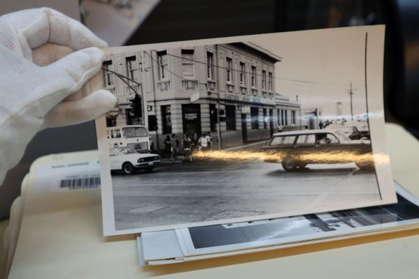 a gloved hand holding up a photo over a stack of folders and other photos