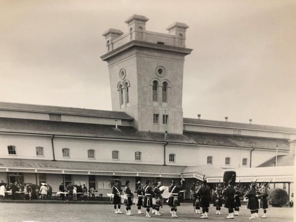 black and white photo of a building with a marching band and gathering crowd outside.