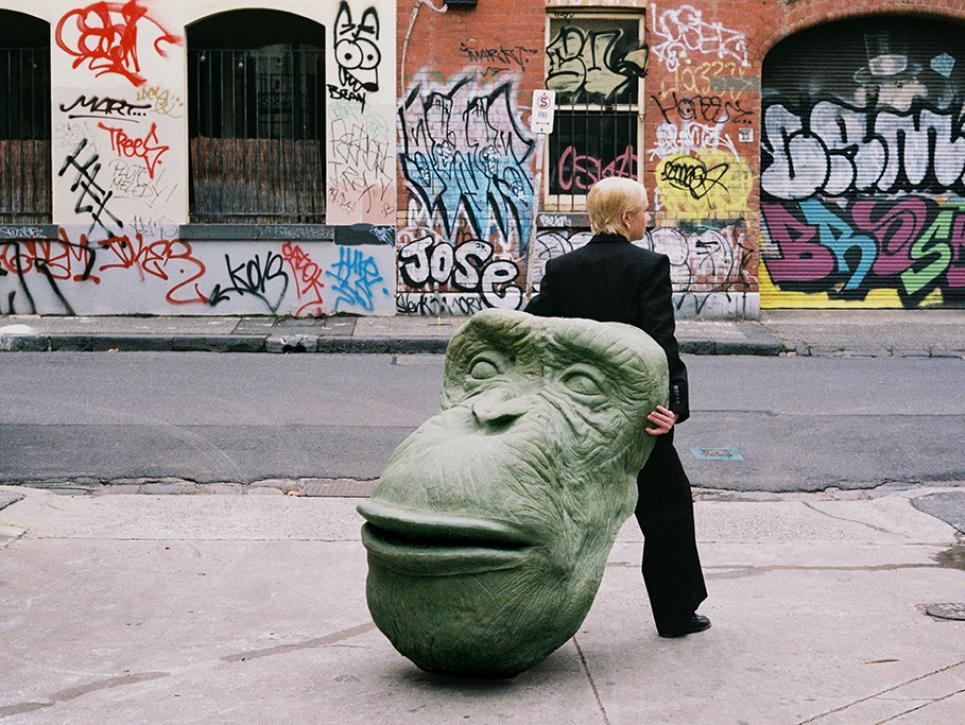 A person drags a large sculpture of a chimpanee head through a Melbourne alleyway.